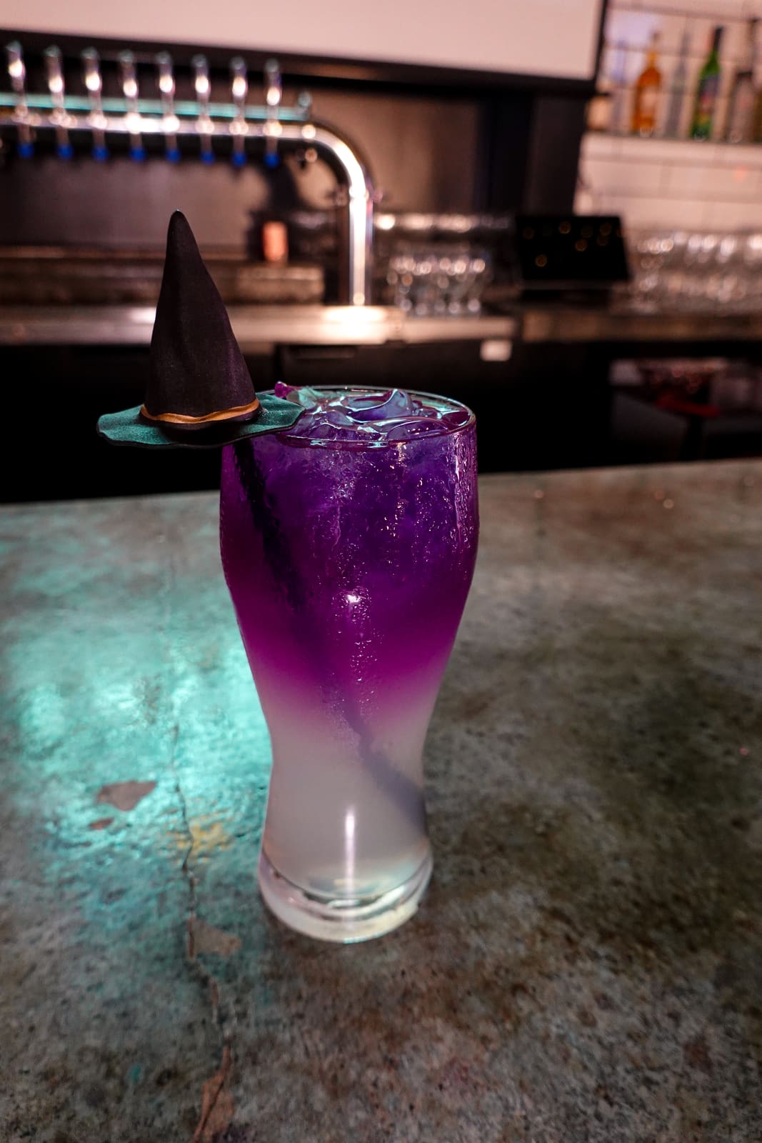 A purple glitter cocktail with a witch-hat garnish on the bar