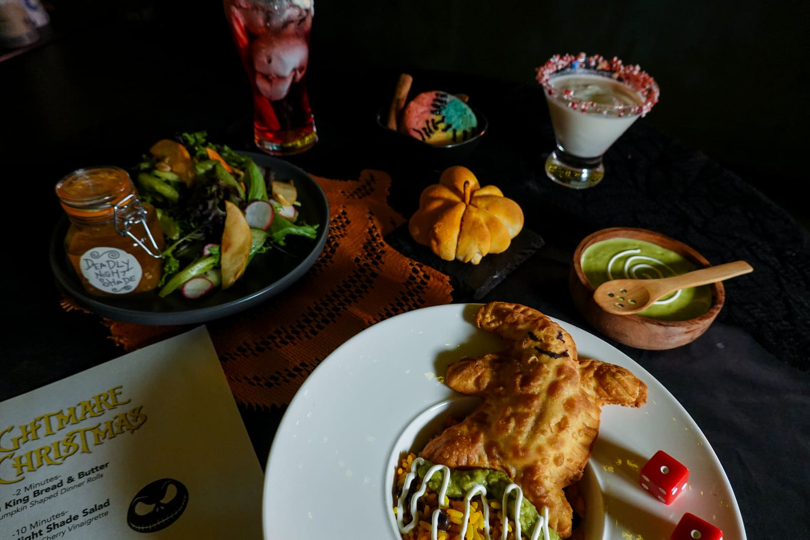 A table spread with pumpkin-shaped pastries, salad and a sugar-rimmed drink