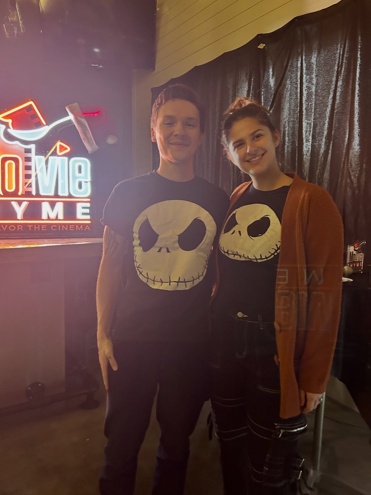 Two guests wearing matching skeleton-print tops beside the Movie Thyme sign