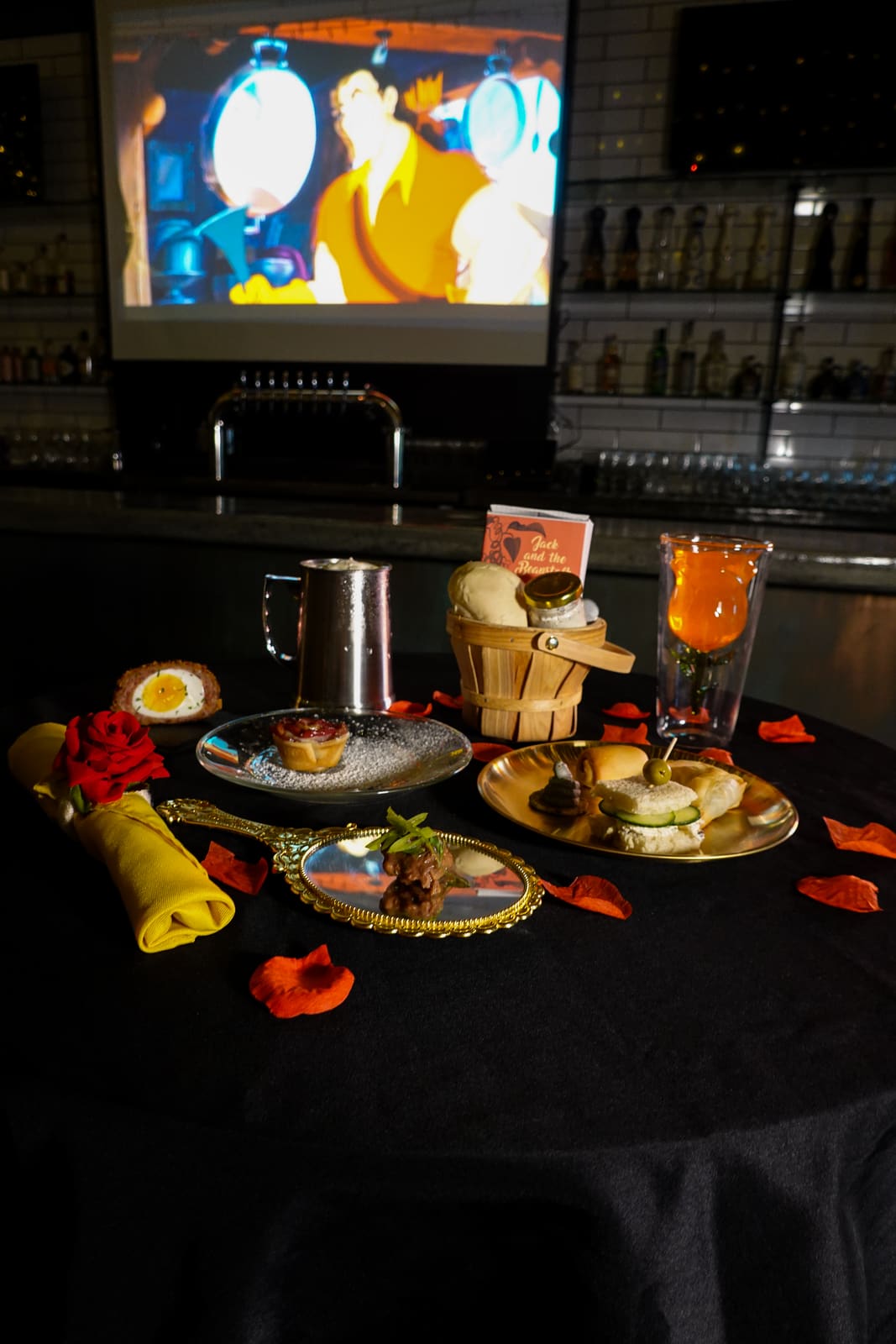 A dressed table with rose petals and Beauty and the Beast playing on the screen behind