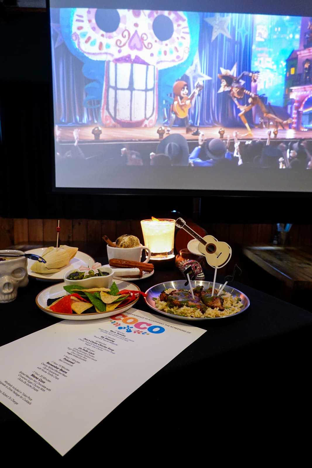 A set table with a candle and Coco playing on the screen behind