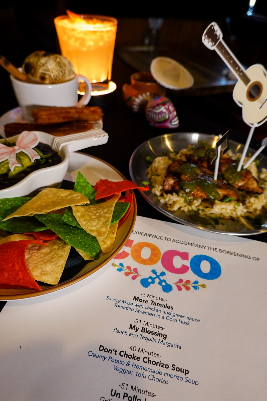 Tortilla chips and guacamole beside a lit candle and the printed Coco menu